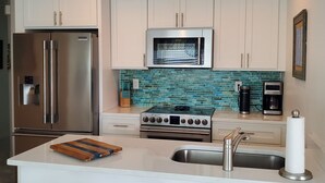 A modern kitchen with white cabinets, stainless steel appliances, a tiled backsplash, and a central island with a sink and a wooden cutting board. - Double Waterfront Property with Amazing Views & Private Pool (Hernando Beach)