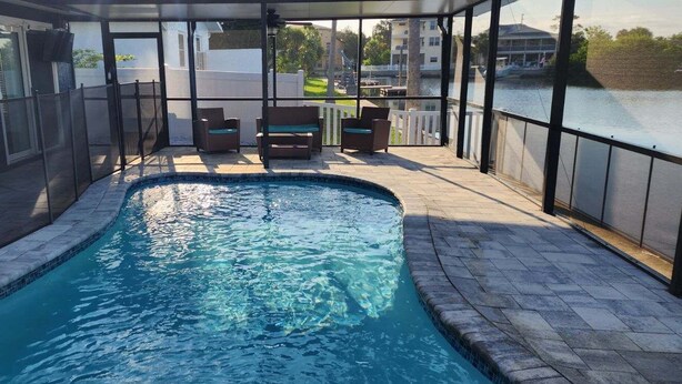An indoor swimming pool with a glass enclosure, seating area, and a view of a body of water. - Double Waterfront Property with Amazing Views & Private Pool (Hernando Beach)