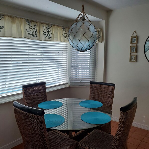 A dining area with a glass table surrounded by wicker chairs, blue cushions, and a hanging light fixture. - Double Waterfront Property with Amazing Views & Private Pool (Hernando Beach)