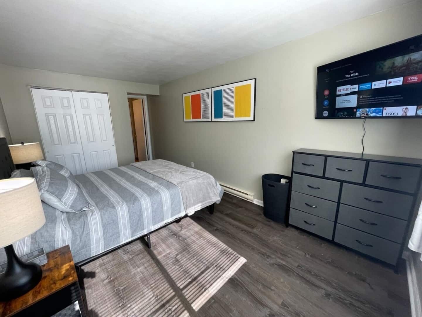 Un dormitorio con una cama, un aparador, un televisor montado en la pared y una puerta.