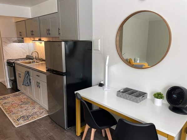 Eine moderne Küche mit Kühlschrank, Herd und Spüle. Ein Esstisch mit Stühlen und ein Spiegel an der Wand sind ebenfalls vorhanden.