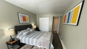 A bedroom with a bed, nightstands, a rug, and artwork on the walls. - Twin Oaks Extended Stay One Bedroom - 2817 Apt 6 (Syracuse)
