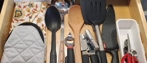 A drawer with various kitchen utensils including a wooden spoon, a black spatula, and a knife.