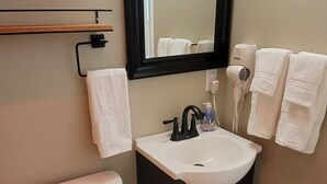 A small bathroom with a toilet, sink, and mirror. There are towels hanging on the wall and a hairdryer on the counter.