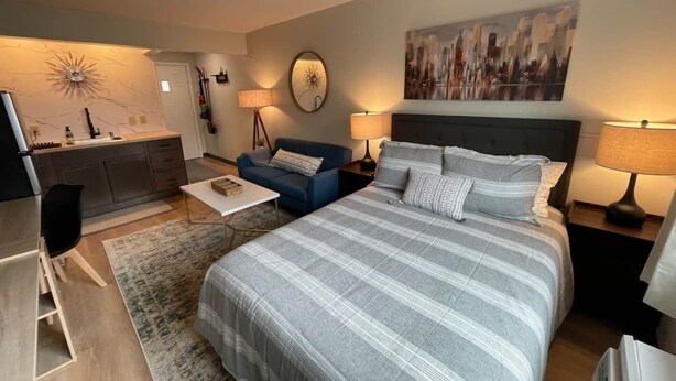 Une chambre à coucher moderne avec un grand lit, un canapé, une petite table et un coin cuisine.