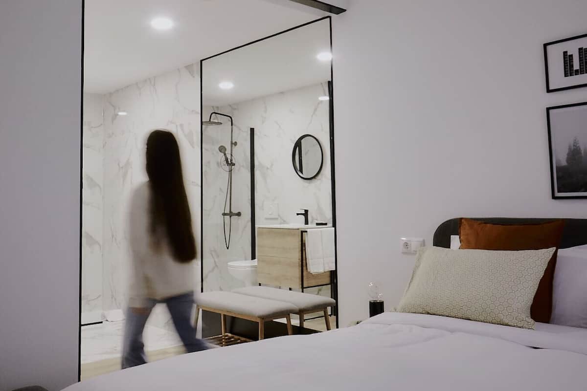 Une chambre d’hôtel moderne avec un grand lit, une tête de lit en bois, une table de chevet et un miroir.