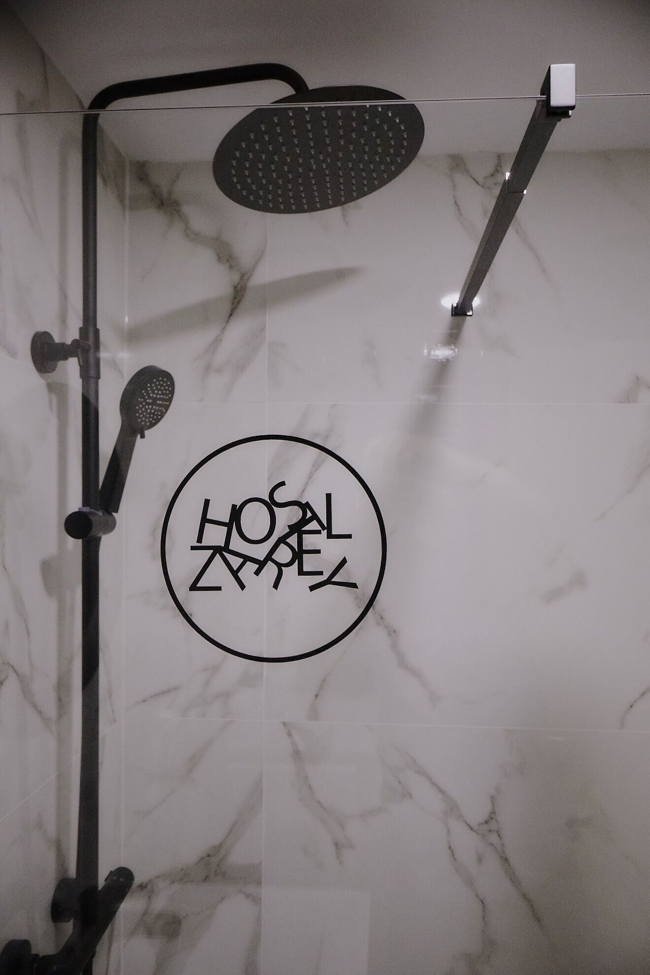 A shower with a circular logo on the wall, a handheld showerhead, and a wall-mounted showerhead.