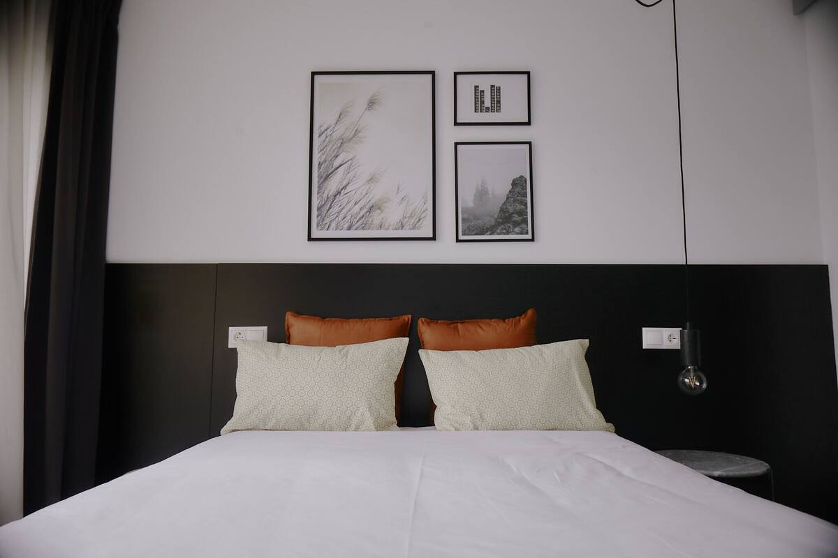 Une chambre d’hôtel moderne avec un grand lit, deux oreillers, une table de chevet et trois tableaux encadrés au mur.