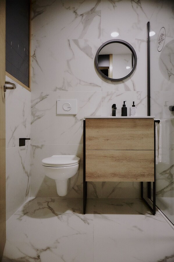 A bathroom with a marble wall, a wooden vanity, a toilet, and a round mirror. - ZAREY HOSTEL (Oleiros)
