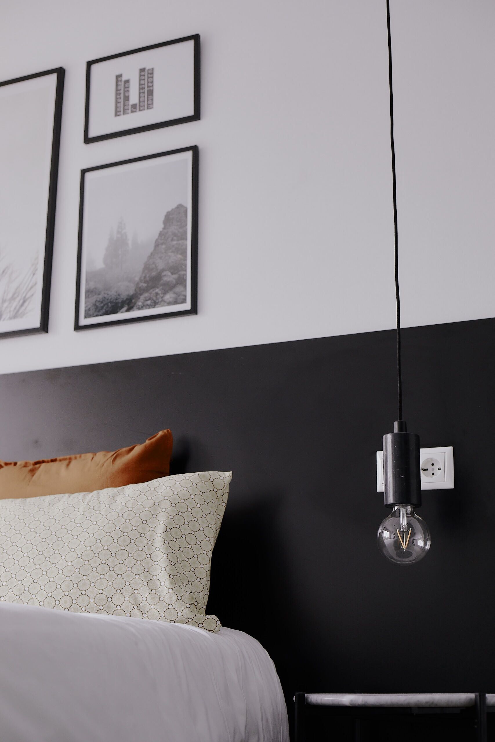 Une chambre à coucher avec un lit, un mur noir et blanc et un luminaire suspendu.