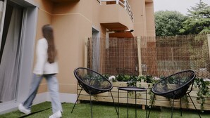 A residential building with a flat roof, balconies, and a small garden area with two black chairs and a table. - ZAREY HOSTEL (Oleiros)