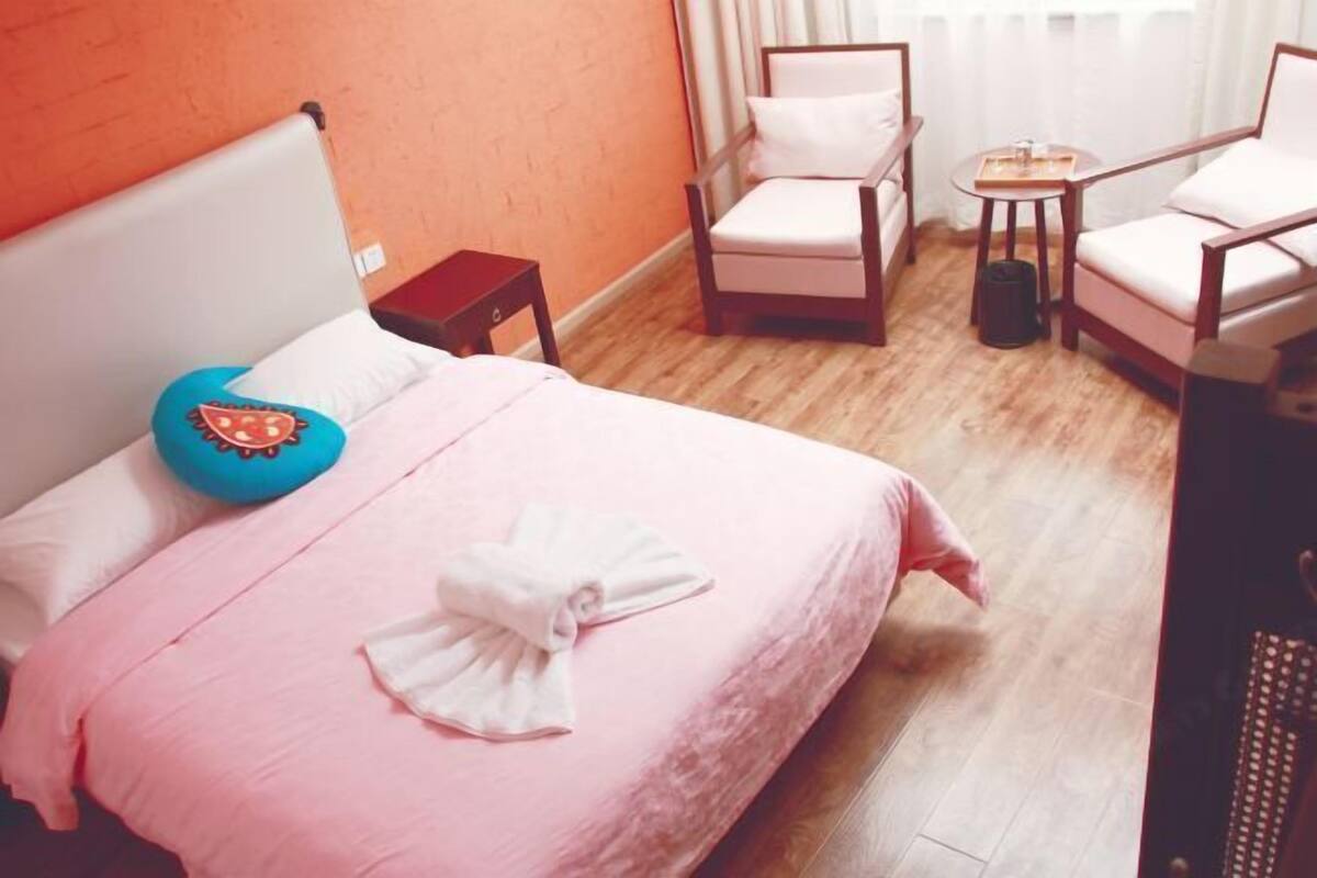 Quarto com cama, cadeira, mesa pequena e janela com cortinas.