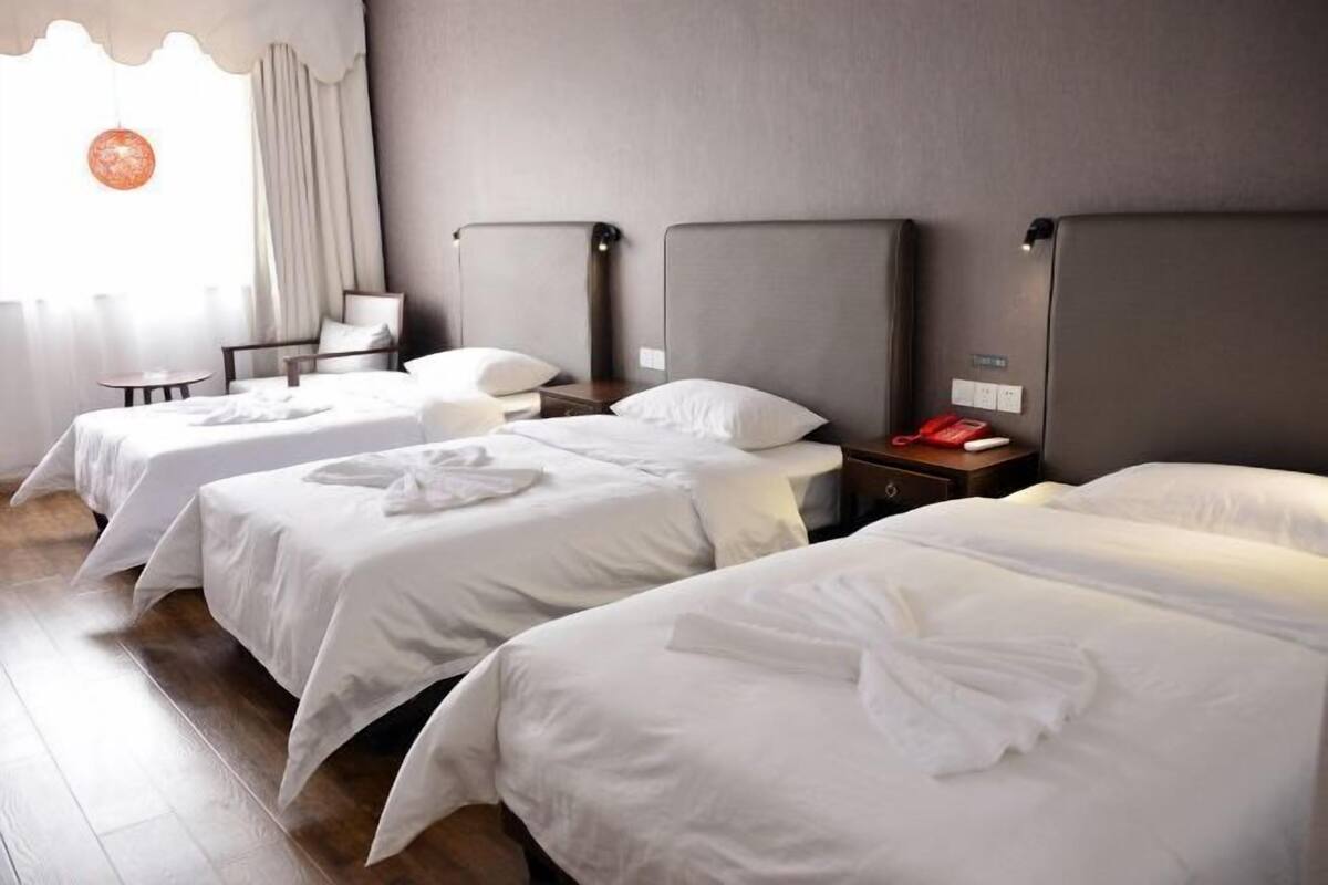 Quarto de hotel com três camas de solteiro, uma mesinha e uma cadeira.