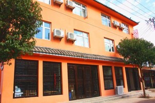 Un edificio con varias ventanas, unidades de aire acondicionado, techo de tejas y un árbol en la parte delantera.