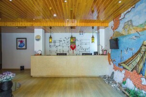 Zona de recepción con techo de madera, un mostrador de recepción y un mural en la pared.