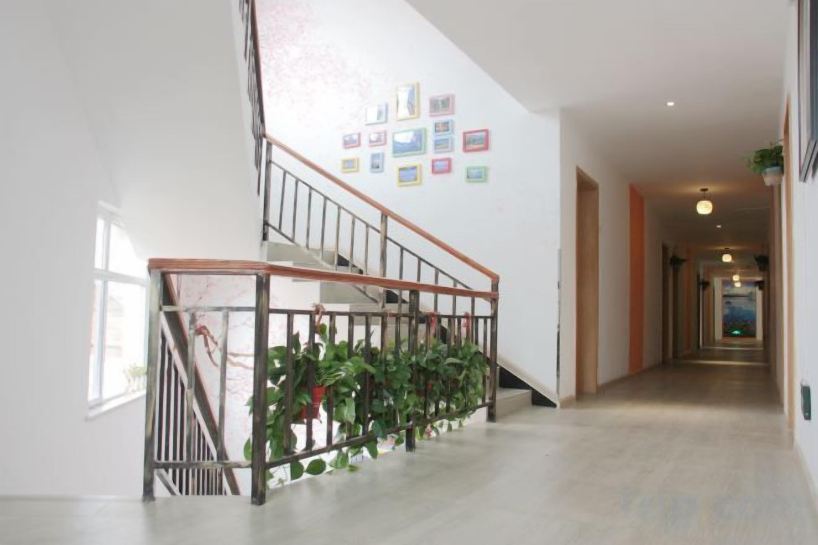 A staircase with a metal railing, a wall with framed pictures, and a hallway leading to a door.