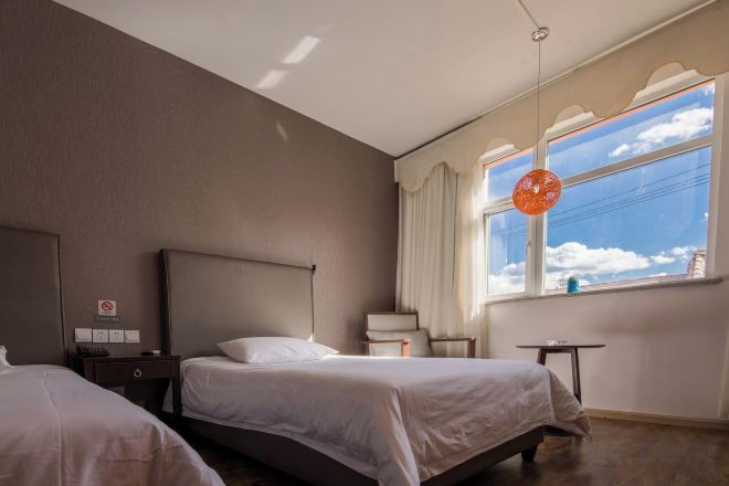 Ein Hotelzimmer mit zwei Betten, einem Schreibtisch, einem Stuhl und einem Fenster mit Blick zum Himmel.