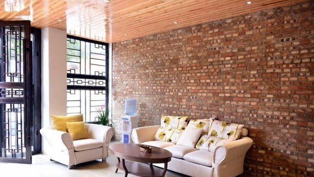 A modern living room with a brick wall, two sofas, a coffee table, and a large window with a geometric design. - Luguhu Aishang Hotel (Ninglang)