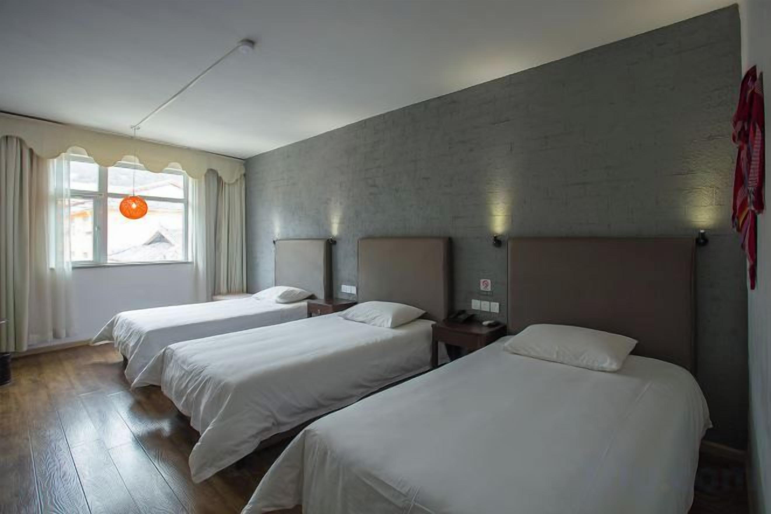 A hotel room with three single beds, a large window with curtains, and a brick wall.
