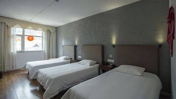 A hotel room with three single beds, a large window with curtains, and a brick wall.