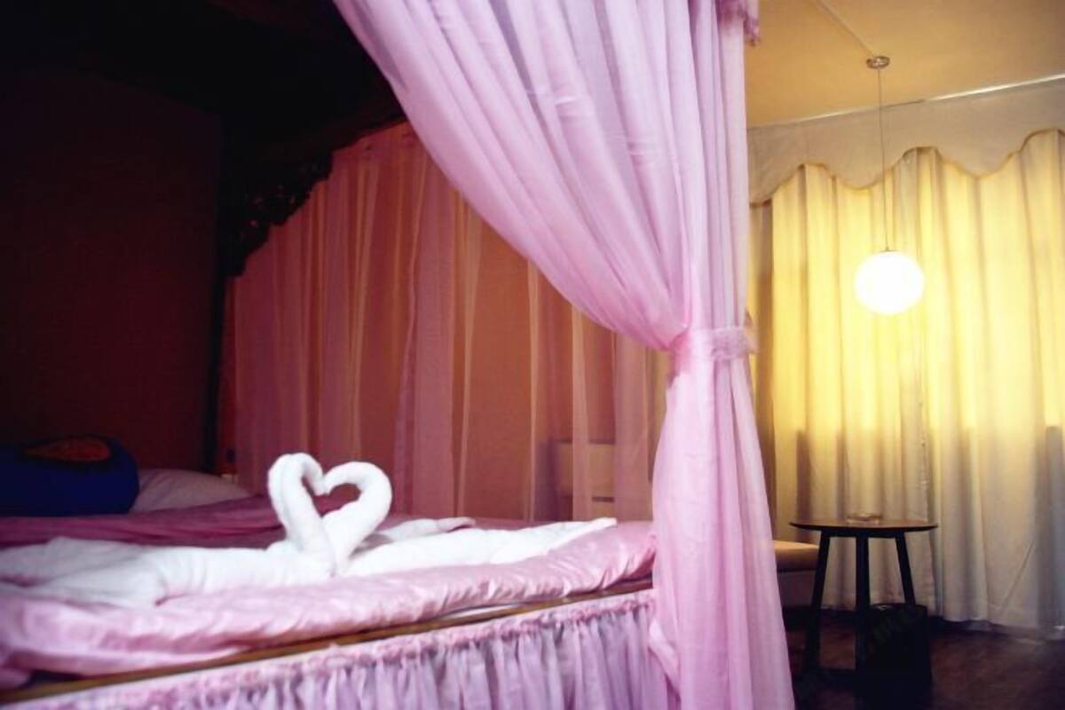Quarto com cama, uma mesinha e luminária suspensa.