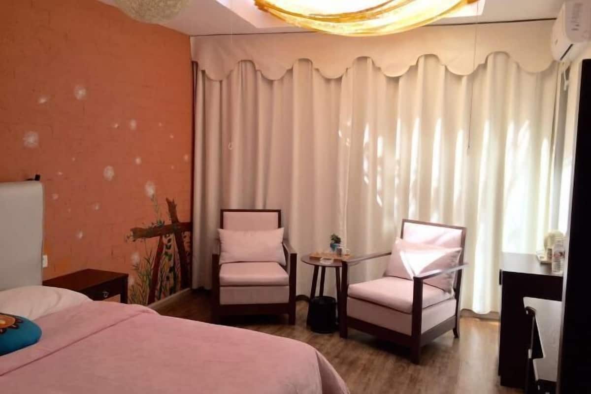 Quarto de hotel com cama, duas poltronas, uma mesinha e uma escrivaninha.