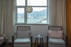 A room with two chairs, a small table, and a window with a view of buildings and mountains.