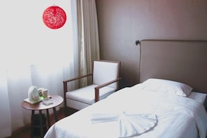 Habitación de hotel con una cama, una silla, una mesita con una tetera y tazas, y un farol rojo.