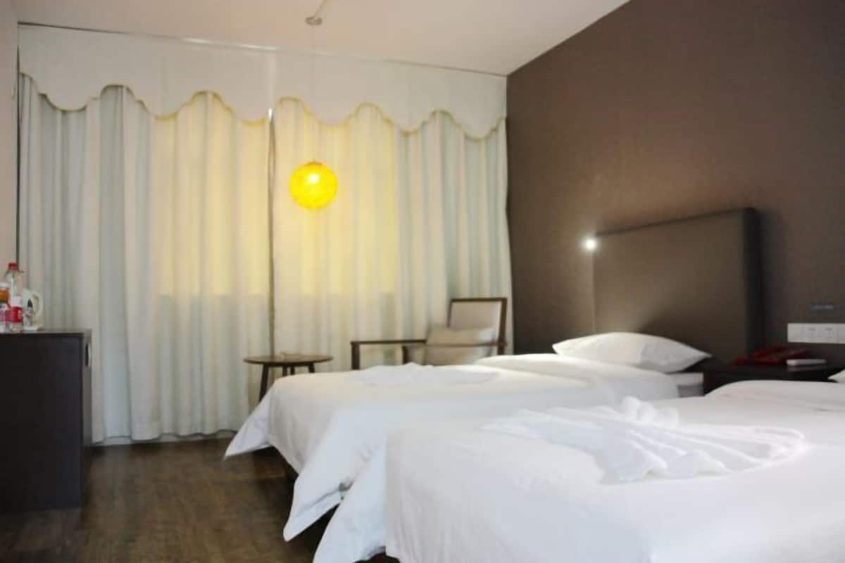 Quarto de hotel com duas camas, uma escrivaninha, uma cadeira e uma janela grande com cortinas.
