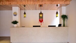 A reception desk with a clock, two potted plants, and three hanging lanterns. - Luguhu Aishang Hotel (Ninglang)