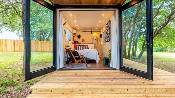 A cozy cabin with a wooden deck, a bed, a chair, and a dining area. - Moss Oak - Container Home Near Magnolia and Baylor (Waco)
