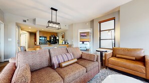 A living room with a sofa, a leather armchair, a dining area, and a kitchen in the background.
