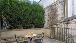 An outdoor patio with a stone wall, a metal fence, and a table set for two with plates of food and drinks.