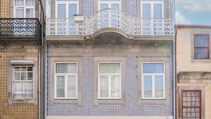 A multi-story building with a tiled facade, large windows, and a balcony with ornate metal railings.