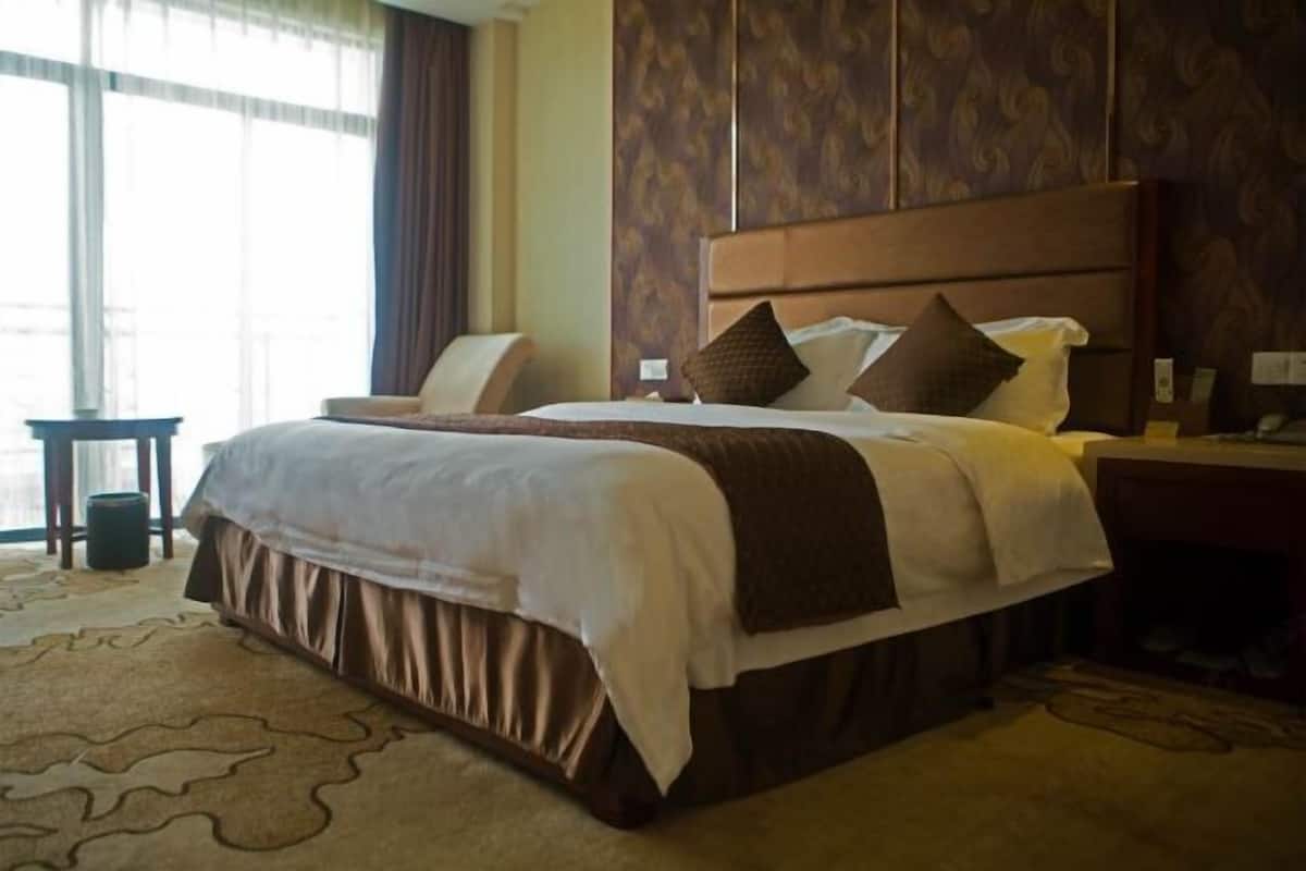 A hotel room with a large bed, a bedside table, a chair, and a view of the outdoors through a window.
