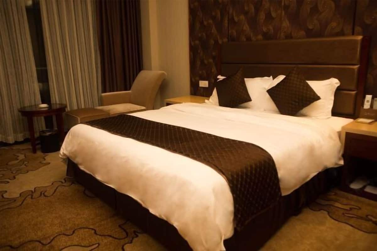 A hotel room with a large bed, a chair, a nightstand, and a carpeted floor.