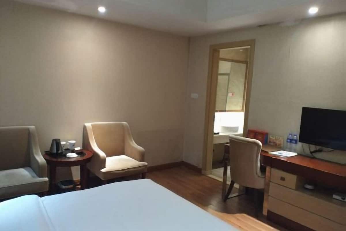 A hotel room with a bed, two armchairs, a desk with a computer, a television, and a small table with a coffee maker.