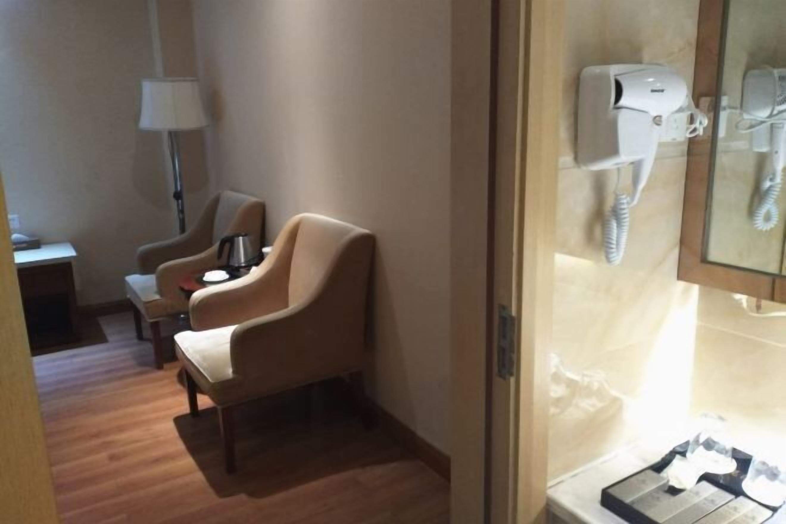 Habitación de hotel con piso de madera, un sillón color beige, una mesita con lámpara y un teléfono.