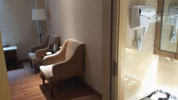 Habitación de hotel con piso de madera, un sillón color beige, una mesita con lámpara y un teléfono.