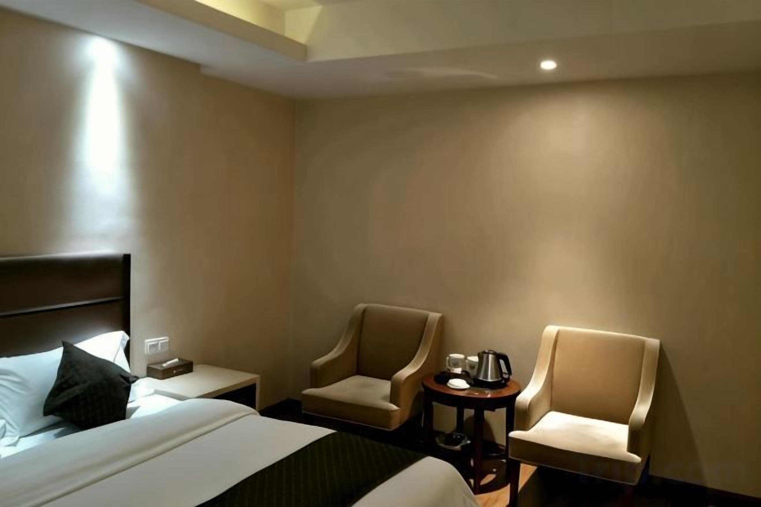 A hotel room with a bed, two armchairs, a small table with a lamp, and a nightstand.