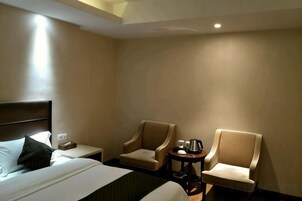 A hotel room with a bed, two armchairs, a small table with a lamp, and a nightstand.