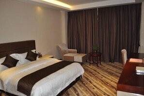 A hotel room with a large bed, a desk, a chair, and a small table with a plant. - Joy Hotel (Fengkai)