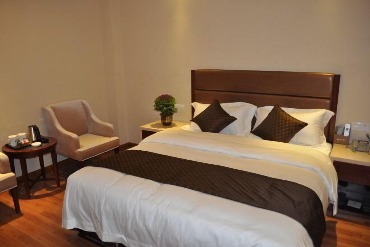 A neatly arranged hotel room with a large bed, a bedside table, a chair, and a small table with a vase of flowers.