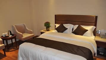 Habitación de hotel impecable con una cama grande, una mesita de noche, una silla y una pequeña mesa con un florero.