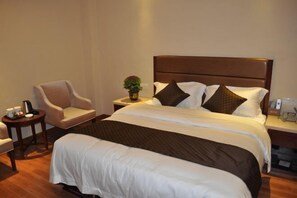 A neatly arranged hotel room with a large bed, a bedside table, a chair, and a small table with a vase of flowers. - Joy Hotel (Fengkai)