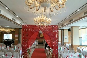 Un salón de banquetes con un arco rojo, candelabros y mesas redondas.