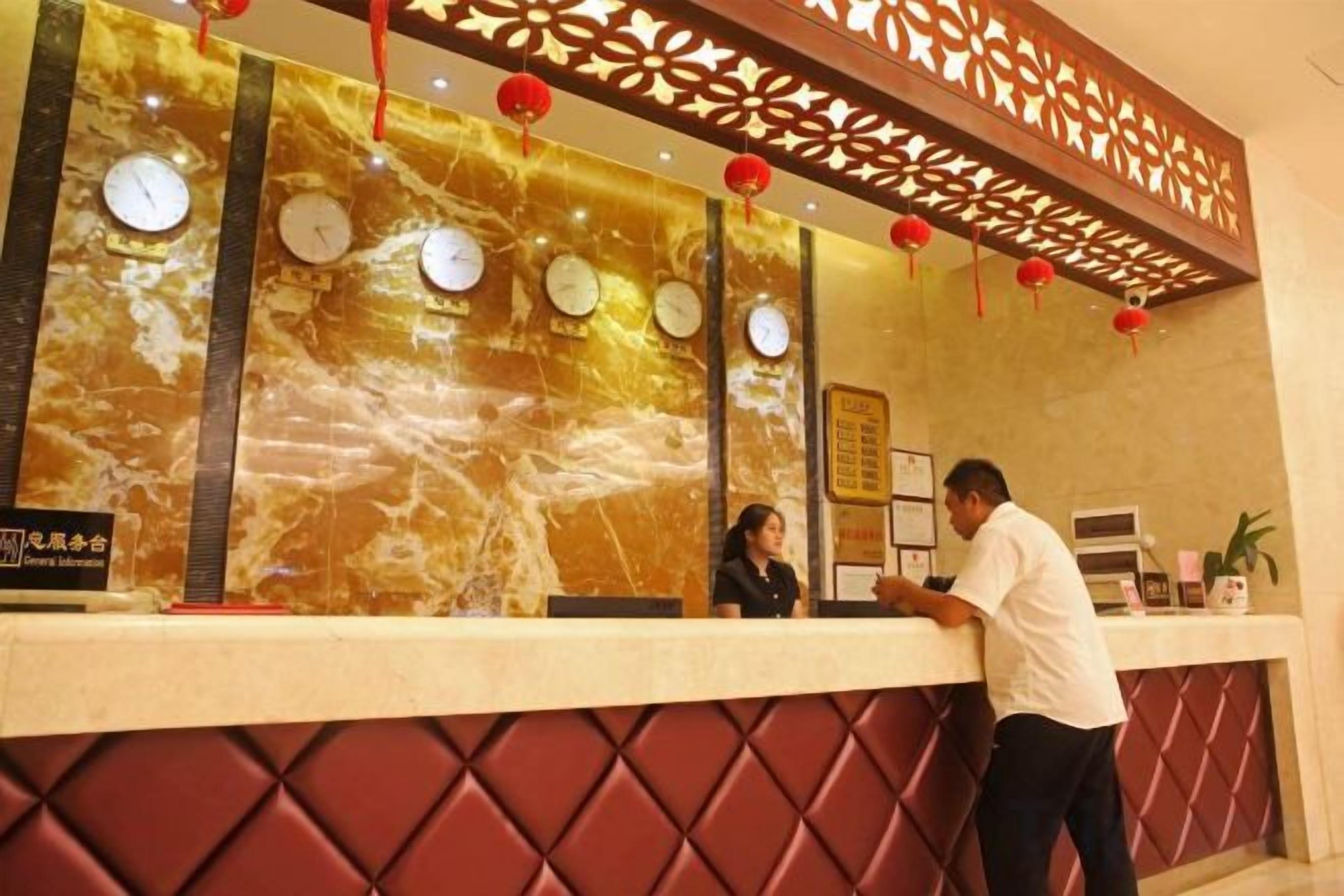 Una recepción de hotel con relojes, una pared decorativa y una zona de estar con cojines rojos.