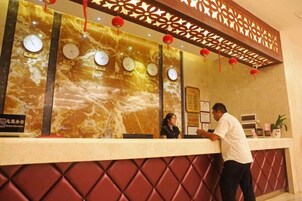 A hotel reception desk with clocks, a decorative wall, and a red cushioned seating area.