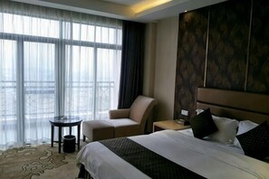 A hotel room with a large bed, a chair, a small table, and a view through sheer curtains. - Joy Hotel (Fengkai)