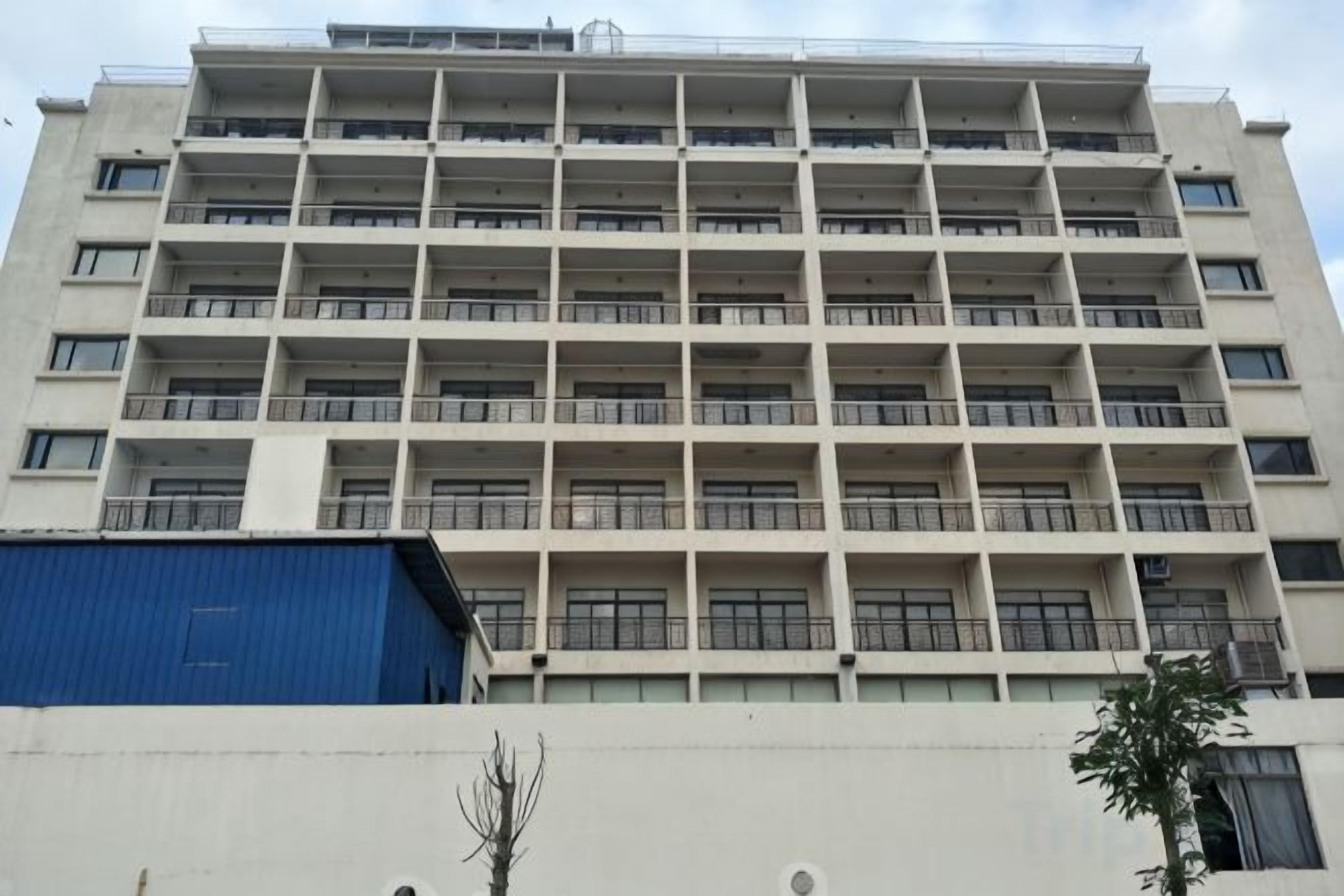 Un edificio de varios pisos con balcones, fachada plana y una estructura azul a la izquierda.